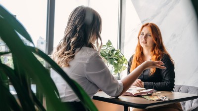 Zwei Frauen sitzen an einem Tisch un unterhalten sich.