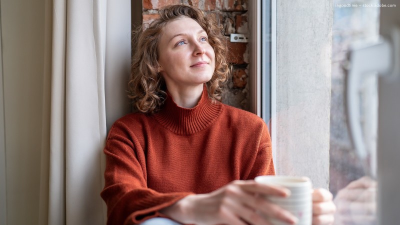 Frau mit Tasse in der Hand schaut aus dem Fenster