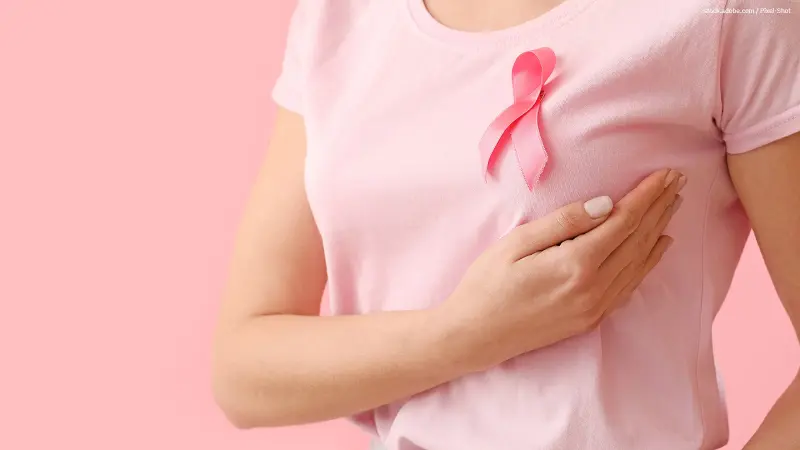 Frau im rosa T-Shirt mit Rosa Schleife tastet Brust ab.