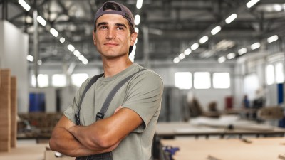 Junger Mann steht in einer Produktionshalle in Arbeitsuniform