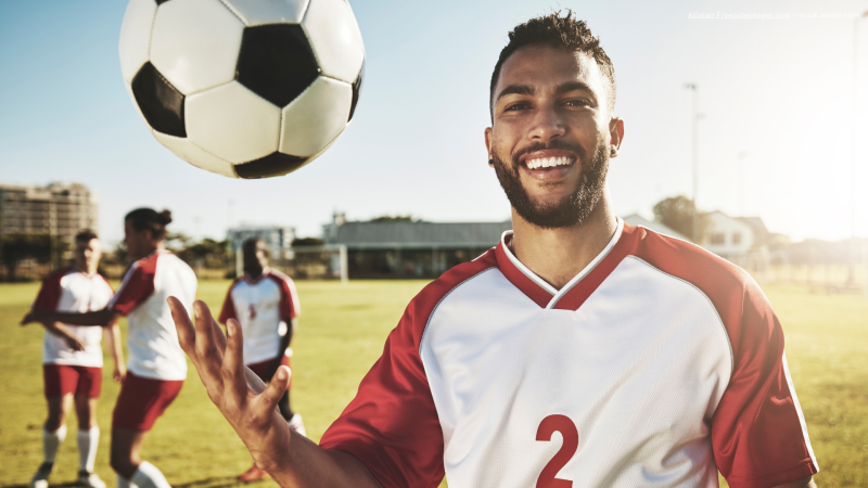 Mann mit Fußball und weiteren Männern im Hintergrund