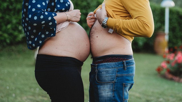 Schwangere Frau und Mann stehen mit dem Bauch einander gegenüber.