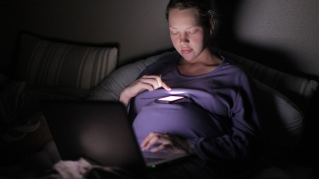 Schwangere Frau im Dunklen am Handy.