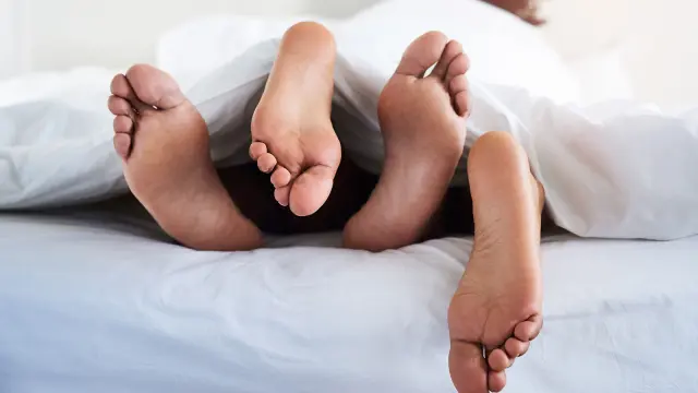 Füße schauen unter der Bettdecke hervor.