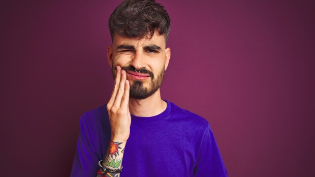 Junger Mann fasst sich an seine Backe und verzieht schmerzhaft das Gesicht.