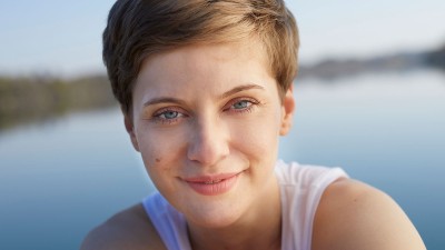 Frau mit einem Muttermal auf der Wange lächelt in die Kamera.