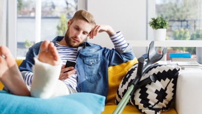 Junger Mann mit Beinbruch und Krücken nutzt Smartphone