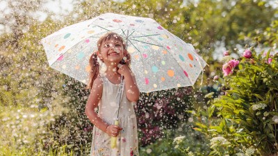 Glückliches Mädchen steht im Sommerregen unter einem Regenschirm