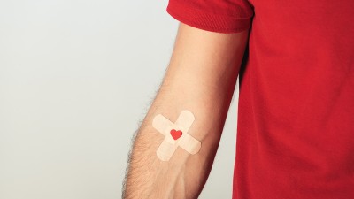 Der Arm eines Mannes mit einem Pflaster mit Herzaufdruck in der Armbeuge.