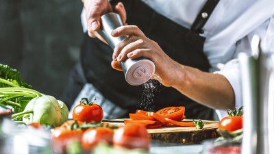 Ein junger Mann würzt Tomaten, daneben anderes Gemüse