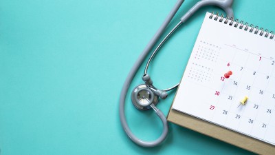 Auf einem hellblauen Hintergrund liegen ein Stethoskop und ein Kalender mit Pins als Symbol für einen Termin beim Arzt.