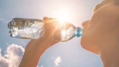 Eine Frau steht im Freien unter der Sonne und trinkt Wasser aus einer Flasche.
