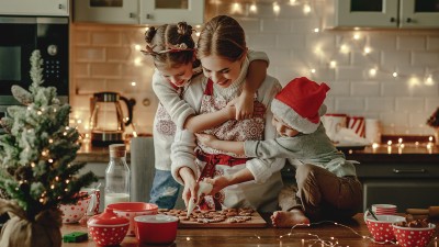 Mutter mit zwei Kindern, die gemeinsam in einer festlich geschmückten Küche Plätzchen backen.
