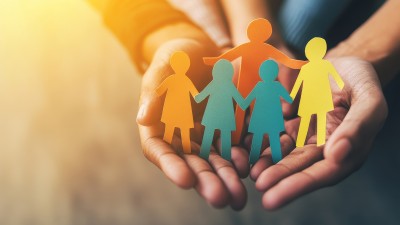 Hände halten eine Gruppe aus bunten Papierfiguren, symbolisch für Familie, Schutz und Versicherung.