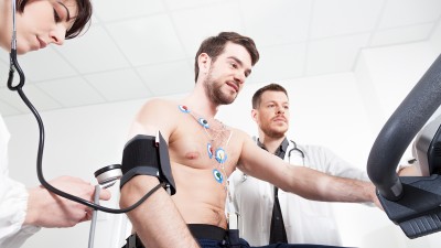 Ein Mann auf einem Ergometer während einer sportmedizinischen Untersuchung mit EKG und Blutdruckmessung.Leistungsdiagnostik beim SportCheck: Mit EKG und Blutdruckmessung gesundheitliche Risiken ausschließen und sicher trainieren.