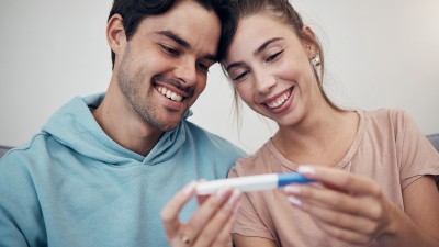 Ein junges Pärchen blickt glücklich auf einen Schwangerschaftstest.