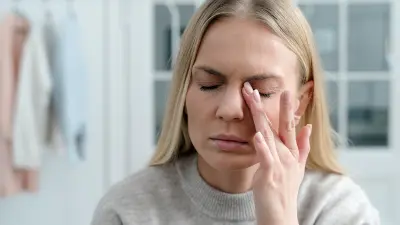 Eine junge Frau, die müde aussieht, fasst sich ans geschlossene Auge.