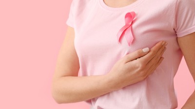 Eine Frau mit pinker Schleife auf dem Shirt tastet ihre Brust ab.