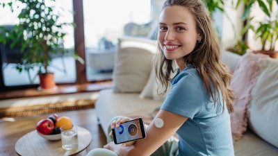 Eine junge Frau misst ihren Zuckerwert über einen Sensor am Arm.