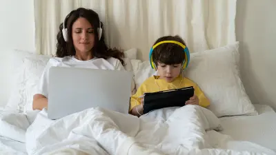 Mutter und Sohn sitzen mit Laptop und Tablet im Bett.
