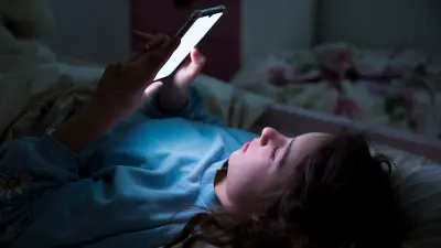 Junge liegt im Dunkeln im Bett und ist am Handy