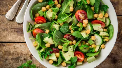 Ein gemischter grüner Salat steht in einer weißen Schüssel auf dem Tisch.