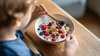 Ein Kind sitzt vor einer Schüssel Joghurt mit Beeren.