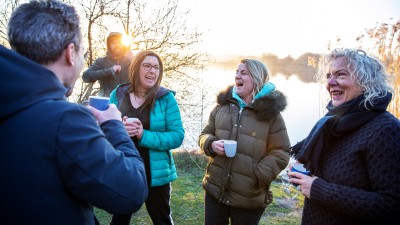 Eine Gruppe von Menschen steht lachend am Seeufer.