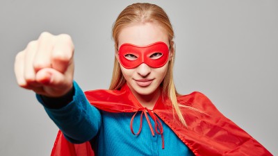 Eine Frau im Superhelden-Kostüm reckt mit entschlossenem Blick die Faust in die Höhe