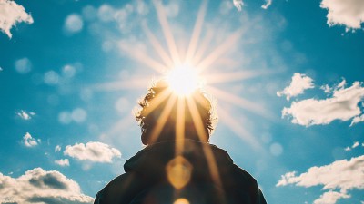 Eine Person steht mit dem Rücken zur Kamera und schaut zur Sonne in den Himmel.