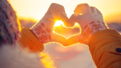 Eine Frau formt mit ihren Fingern ein Herz vor der untergehenden Wintersonne.