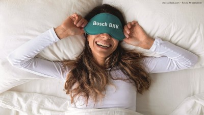 Frau mit Bosch BKK Schlafmaske liegt lachend im Bett