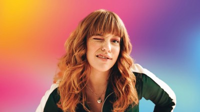 Junge Frau, die mit einem Auge zwinkert, vor buntem Hintergrund in Regenbogenfarben