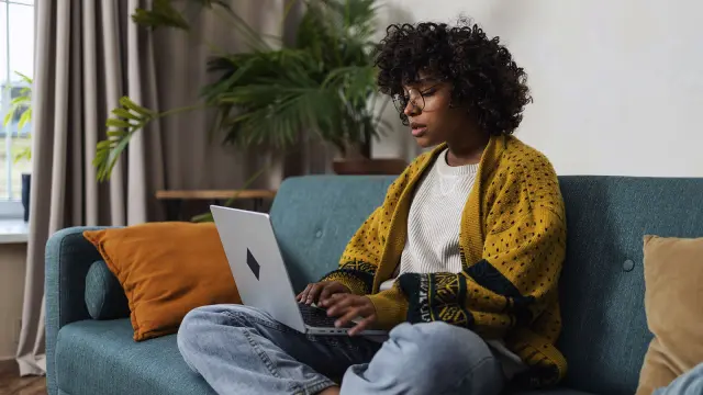 Junge schwarze Frau, mit Laptop auf dem Sofa sitzend
